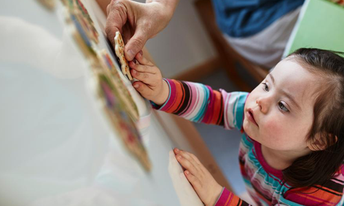 Widerspruch Ein Kind setzt ein Puzzle-Teil in eine Wand und bekommt dabei Unterstützung.