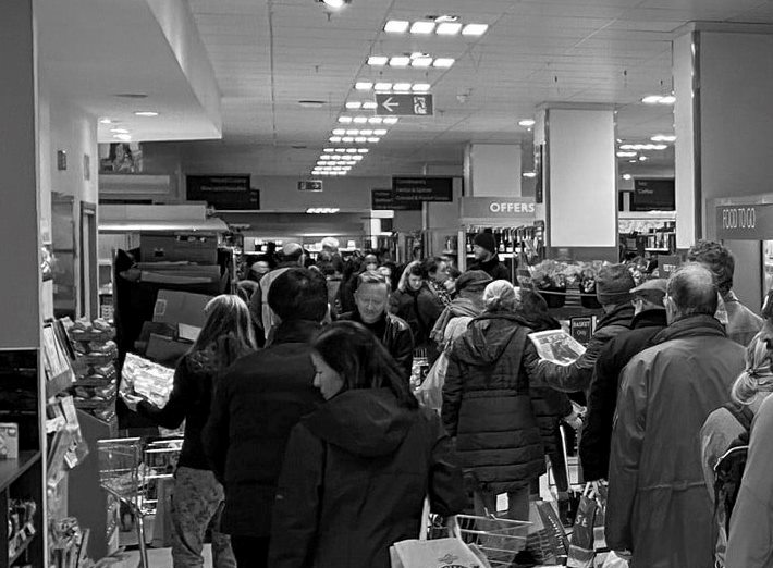 Farbentsättigtes Foto einer langen Reihe von Supermarktkunden vor der Kasse.