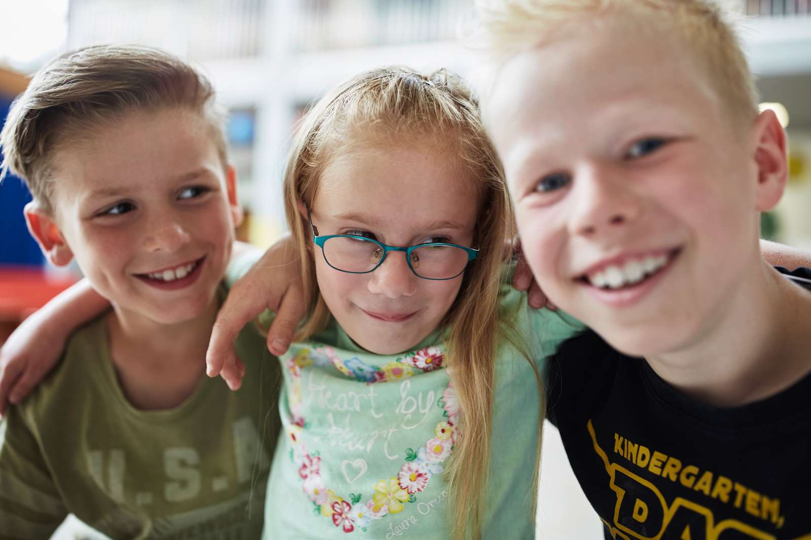 Zwei kleine Jungen und ein kleines Mädchen - in Schulterumarmung und lachend.