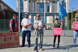 Rolf Flathmann, Stellvertretender Bundesvorsitzender, spricht auf der Demo für die Petition "Teilhabe ist kein Luxus" vorm Bundeskanzleramt. Die weiteren Personen auf dem Bild, von links:Christian Keitmann, Marcus Dengler, Philipp Grossmann (alle drei Selbstvertreter der Lebenshilfe Altmühlfranken), Katja Macheleidt, Büro für Selbstvertretung der Lebenshilfe Berlin, Sascha Ubrig, hauptamtlicher Selbstvertreter der Lebenshilfe Berlin, und Anja Hahlweg, Büro für Selbstvertretung der Lebenshilfe Berlin.
