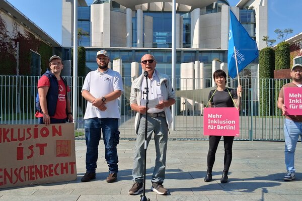 Rolf Flathmann, Stellvertretender Bundesvorsitzender, spricht auf der Demo für die Petition "Teilhabe ist kein Luxus" vorm Bundeskanzleramt. Die weiteren Personen auf dem Bild, von links:Christian Keitmann, Marcus Dengler, Philipp Grossmann (alle drei Selbstvertreter der Lebenshilfe Altmühlfranken), Katja Macheleidt, Büro für Selbstvertretung der Lebenshilfe Berlin, Sascha Ubrig, hauptamtlicher Selbstvertreter der Lebenshilfe Berlin, und Anja Hahlweg, Büro für Selbstvertretung der Lebenshilfe Berlin.