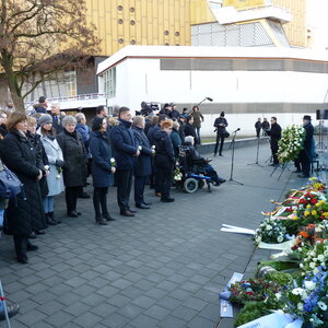 Das Bild zeigt viele Menschen, Kränze mit Blumen vor der blauen Wand der Gedenkstätte in der Berliner Tiergartenstraße.
