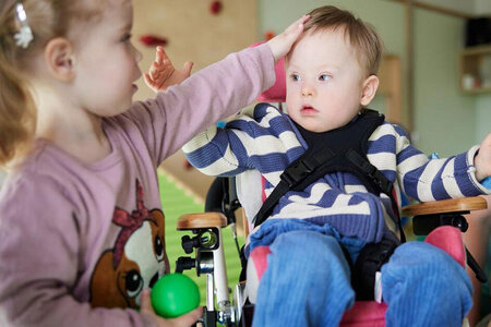Ein kleines Mädchen streichelt einen Jungen, der in einem Rollstuhl sitzt. Der Junge hat eine sogenannte geistige Behinderung.