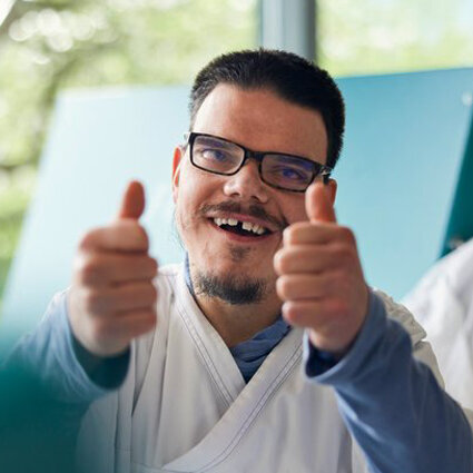 Mitarbeitende mit Behinderung Ein junger Mann mit Beeinträchtigung hebt die Daumen hoch.