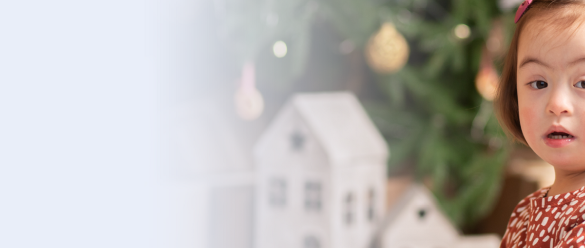 Ein kleines Kind in der Nahaufnahme. In Hintergrund ist ein Weihnachtsbaum zu erkennen.