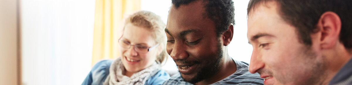 Drei junge Menschen sitzen gemeinsam beisammen und lächeln.