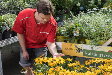 In der dritten toom-Broschüre in Leichter Sprache geht es um Klima- und Naturschutz im Garten und Haushalt. Das Foto zeigt einen jungen Mann zwischen Blumen der Gartenabteilung eines toom-Baumarktes.