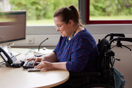 Eine junge Frau mit Beeinträchtigung an ihrem inklusiven Arbeitsplatz.