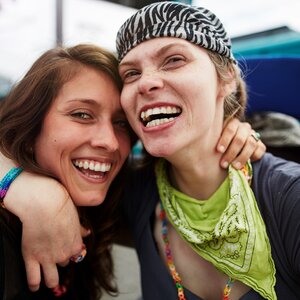 Das Bild zeigt zwei junge Frauen, die sich lachend umarmen. Eine von beiden sitzt im Rollstuhl.