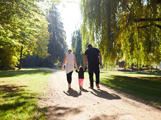 Der Weg zu einer inklusiven Gesellschaft Auf dem Bild sieht man eine kleine Familie von hinten, die gerade einen langen, sonnengefluteten Weg durch einen Park nimmt.