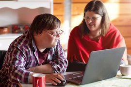 Ein junger Mann mit Down-Syndrom und eine junge Frau sitzen gemeinsam an einem Laptop.