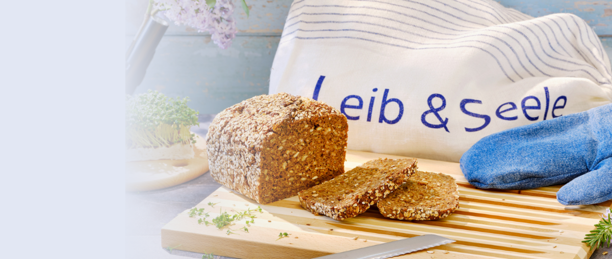 Ein Laib Brot, Ofenhandschuhe, eine Tasse und ein Schneidebrett in einer Nahaufnahme.